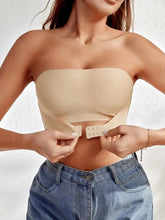 Woman wearing a beige strapless top and blue jeans on a white background